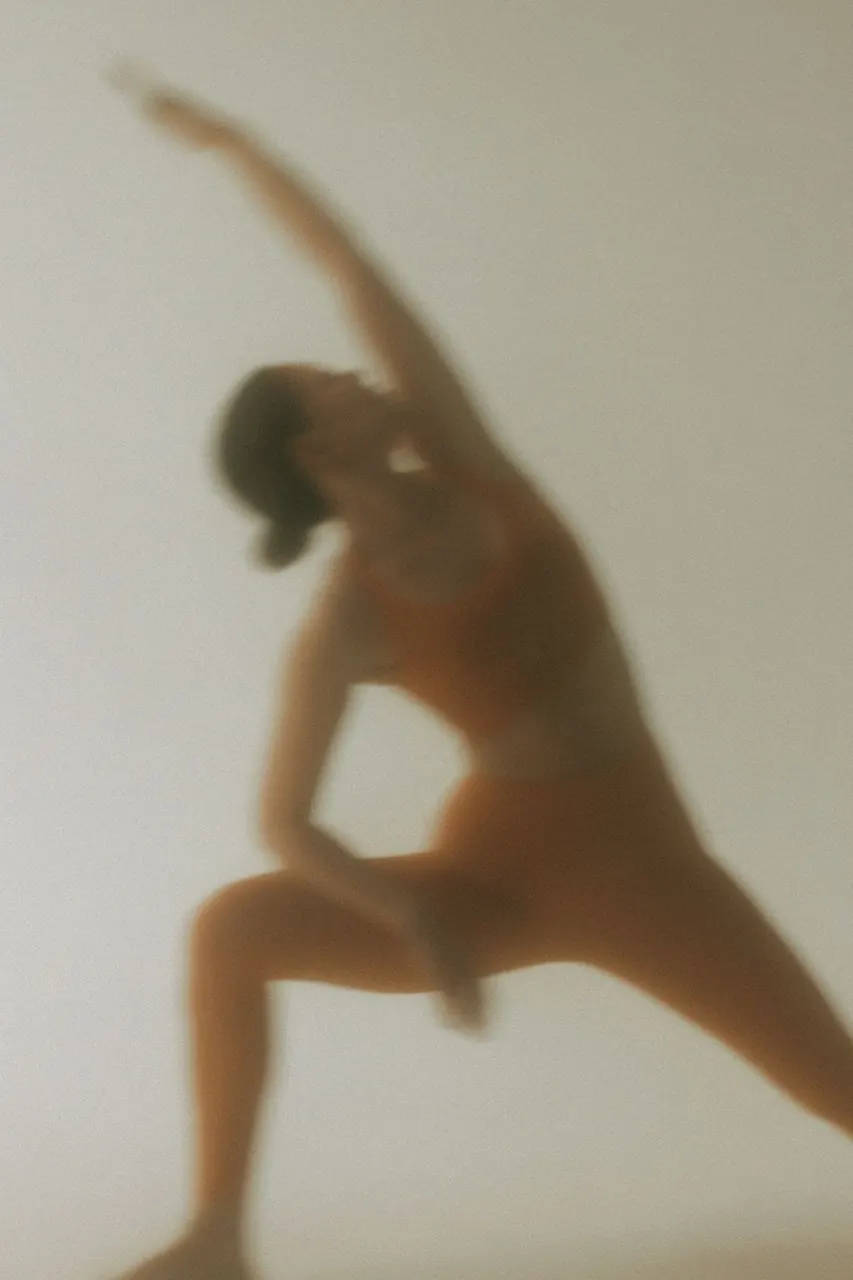 A softly focused yoga practitioner reaching overhead in a standing lunge