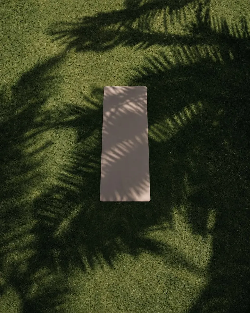 A yoga mat on grass under palm leaf shadows